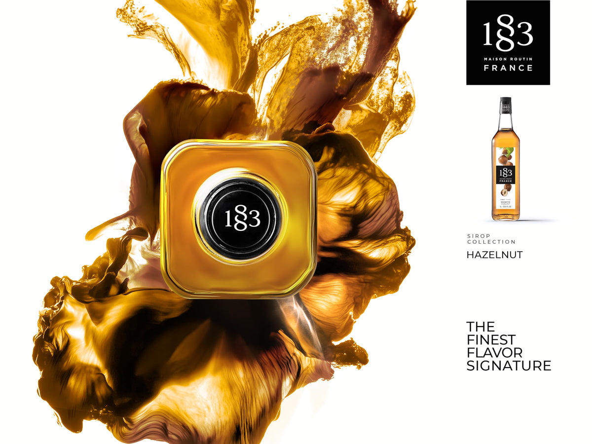 1883 Maison Routin hazelnut syrup being poured into a latte for rich flavor.