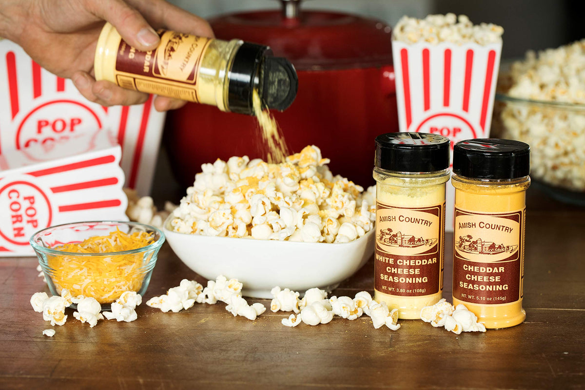 Amish Country Popcorn cheddar seasoning being dispensed onto popcorn for even coverage.
