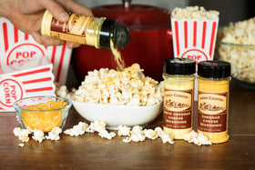 Amish Country Popcorn cheddar seasoning being dispensed onto popcorn for even coverage.