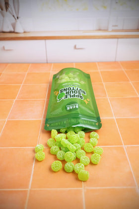 Bear Necessities Sour Buttons apple gummy close-up demonstrates resealable bag preserving freshness.