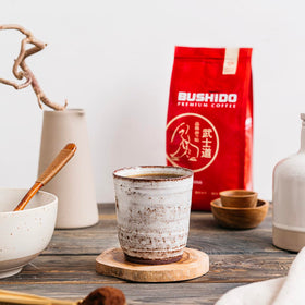 BUSHIDO Red Katana coffee bag beside a steaming mug, inviting tasting.