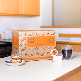 Day To Day Coffee Donut Blend pods beside a Keurig for quick, reliable cups.