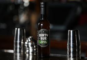 Pouring Dirty Sue olive brine into a martini for depth.