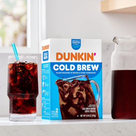 Pouring Dunkin’ Cold Brew over ice in a tall glass.