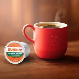 Single-serve Dunkin Decaf pod beside a steaming cup.