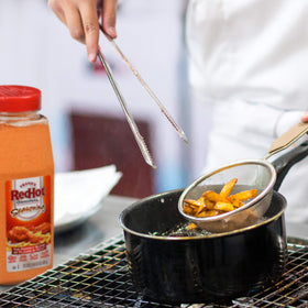 Franks RedHot Original Seasoning shaker next to burgers elevates taste.