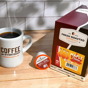 Fresh Roasted Coffee Maple Creme Pod capsule beside a steaming cup.