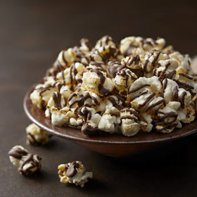 G.H. Cretors Dark Chocolatey Drizzle Popcorn closeup bite, rich chocolate drizzle on fluffy kernels.