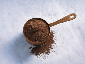 Ghirardelli dark chocolate cocoa powder being poured into hot cocoa showing deep color and aroma.