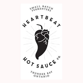Heartbeat KO Edition packaging beside fresh peppers emphasizes gourmet hot sauce.
