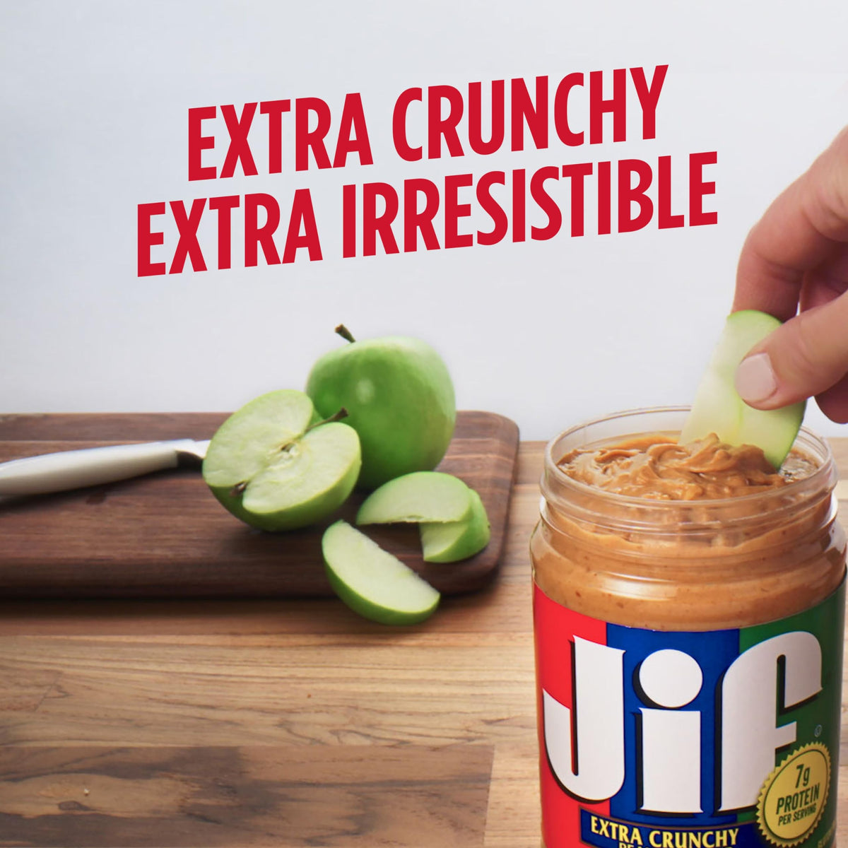 Spoon dipping into Jif Crunchy Peanut Butter reveals visible peanut bits and aroma.