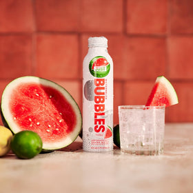 JUST Bubbles Watermelon aluminum-reusable bottle sits beside a glass with ice.