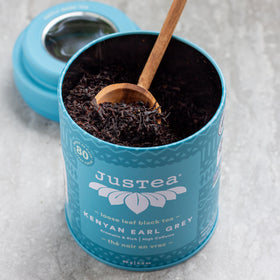 JusTea tin and hand-carved spoon on counter showcasing gift packaging.