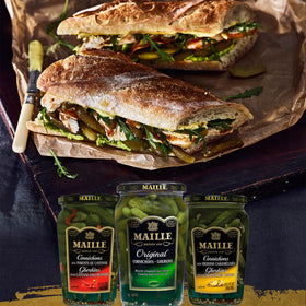 Maille Cornichons Original beside a cheese plate for snacking.