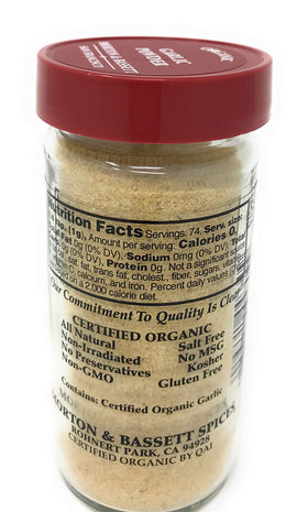 Morton & Bassett Organic Garlic Powder showcased in clear bottle beside fresh herbs.