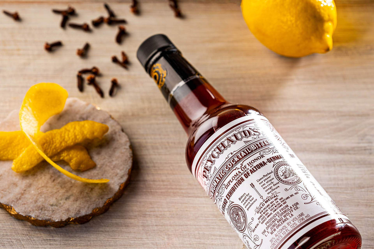 Peychaud's bottle on bar with ingredients for cocktail creation.