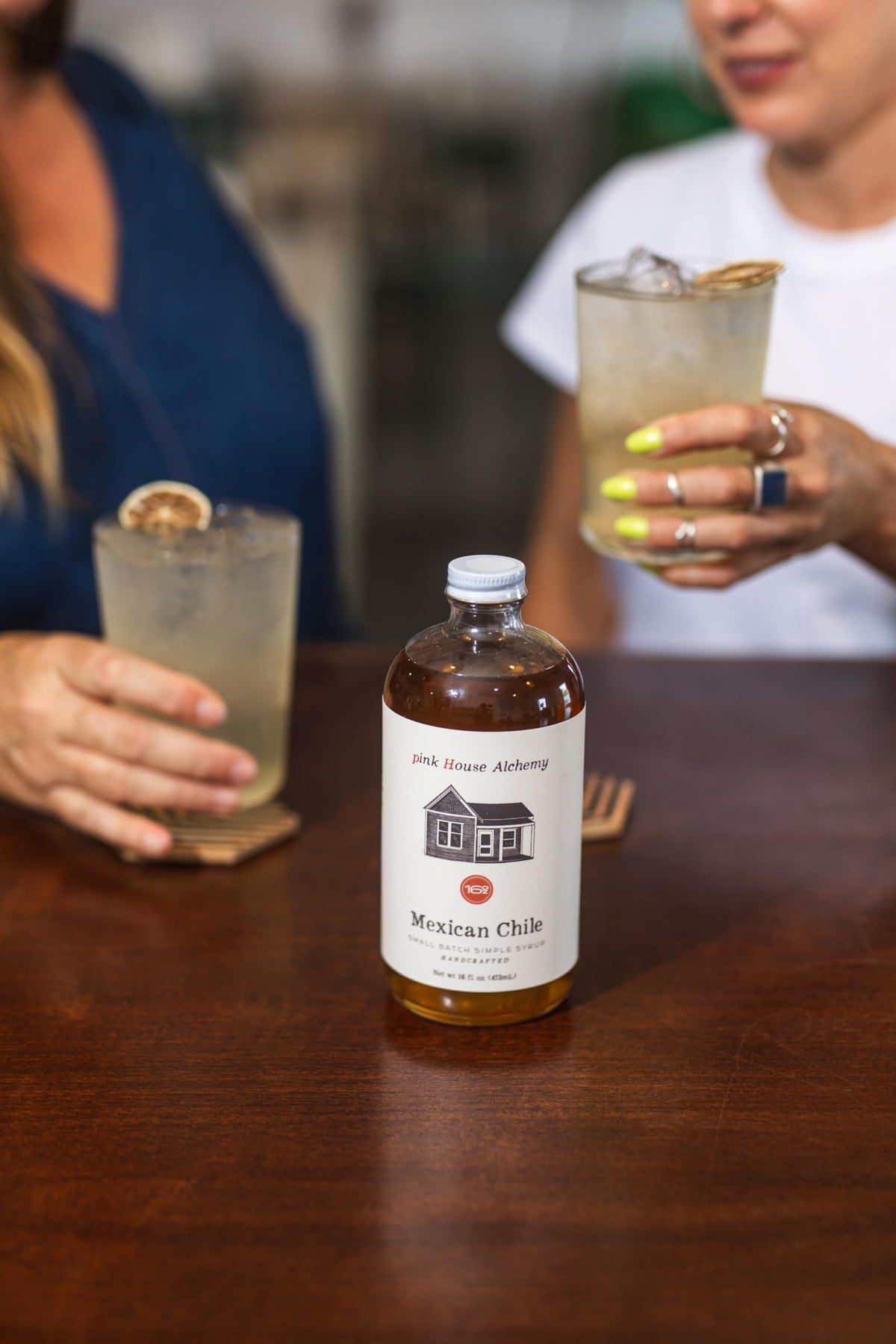 Pouring Pink House Alchemy syrup into a glass for a bright chile-lime twist