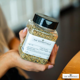 Raw Essentials seasoning bottle beside a grill-ready dish and vegetables.