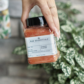 Raw Essentials tomato powder poured from a spoon for precise seasoning.