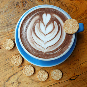 Real Naturals Keto Cookies Butter Coconut plate beside coffee suggests a dessert pairing.