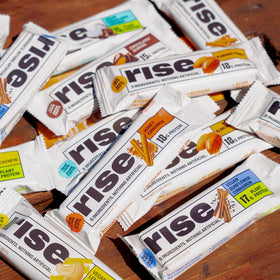 Gym bag-ready Rise bar beside a smoothie for a balanced snack.