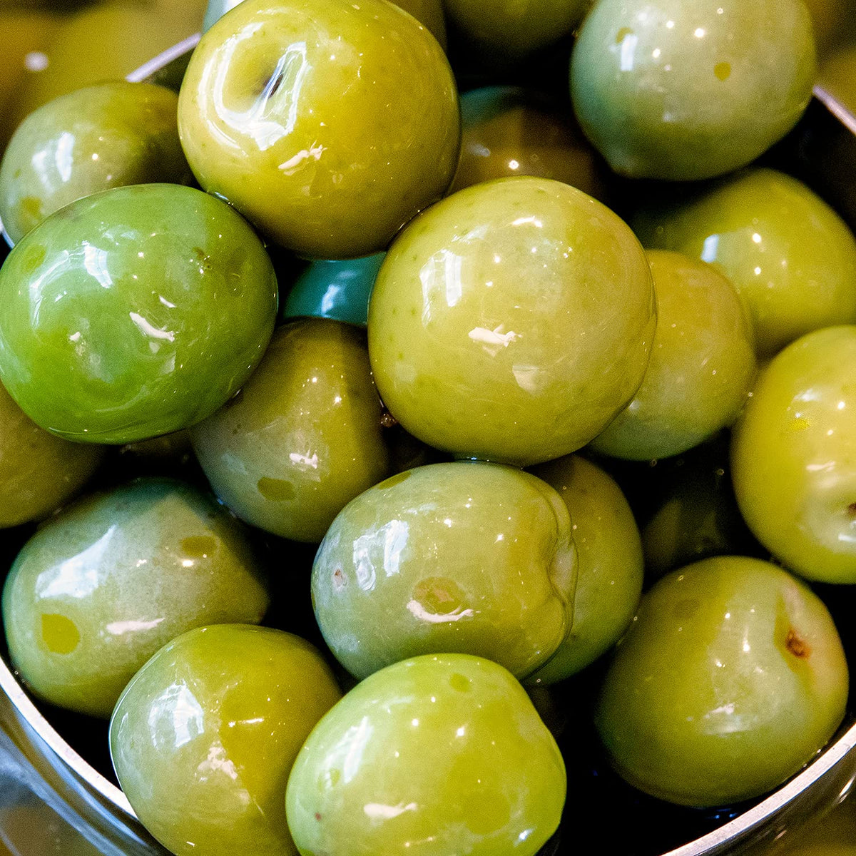 Sanniti olives peek inside the jar, showcasing vibrant green fruit.