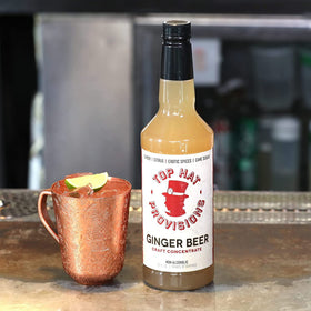 Ginger beer syrup bottle with glasses and lime for a refreshing Moscow Mule.