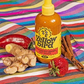 Yellowbird Strawberry Ginger hot sauce being poured over greens
